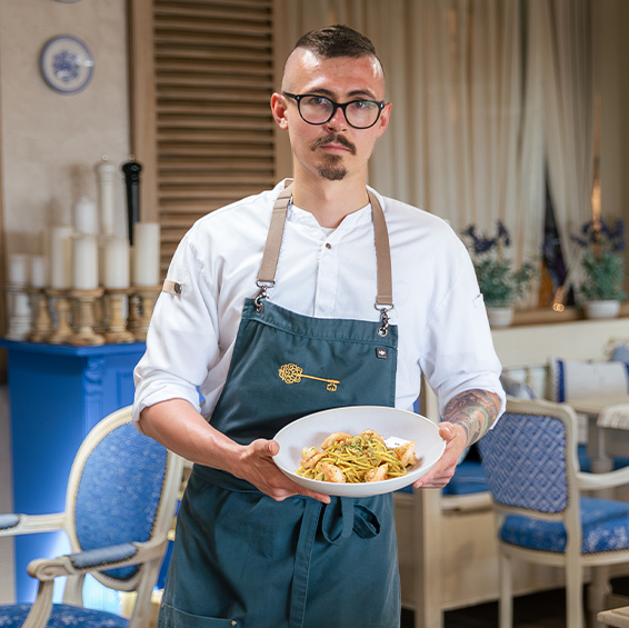 Szef kuchni trzyma talerz ze spaghetti i krewetkami we wnętrzu restauracji 
