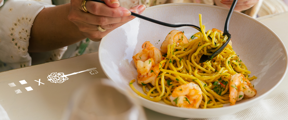 Spaghetti z krewetkami i czarnymi sztućcami w beżowej porcelanowej misce 