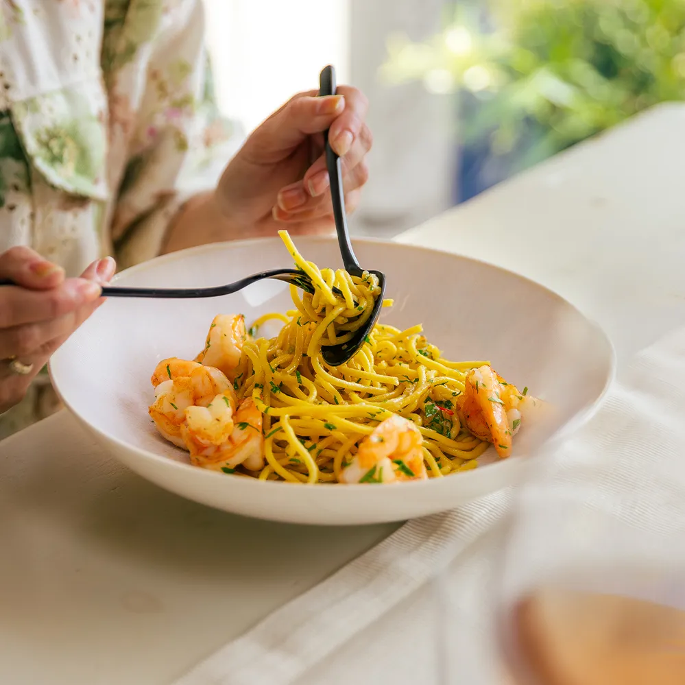 Spaghetti z krewetkami w beżowej misce, nabierane widelcem i łyżką